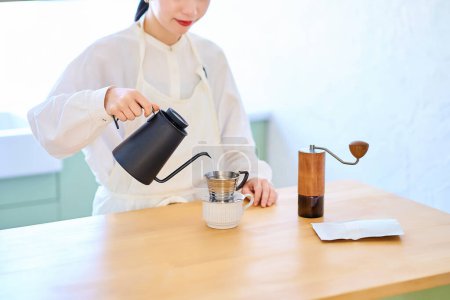 Jeune femme avec tablier faisant du café dans la cuisine