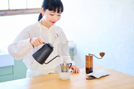 Téléchargez les photos : Jeune femme avec tablier faisant du café dans la cuisine - en image libre de droit
