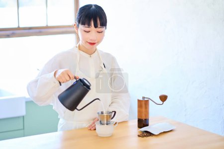 Foto de Mujer joven con delantal haciendo café en la cocina - Imagen libre de derechos