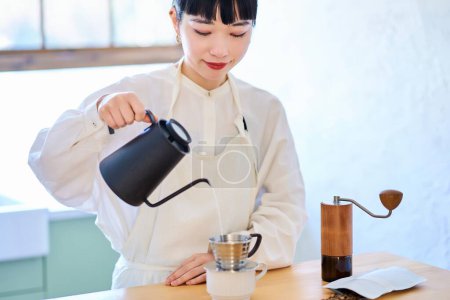 Junge Frau mit Schürze kocht Kaffee in der Küche