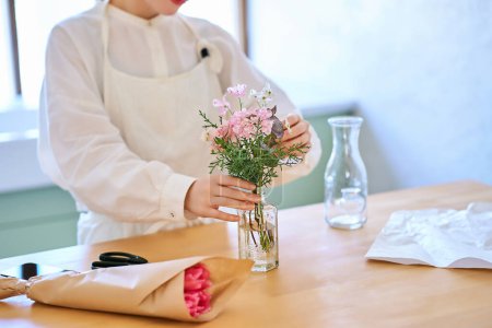 Photo for Young woman enjoying flowers in a vase in the room - Royalty Free Image
