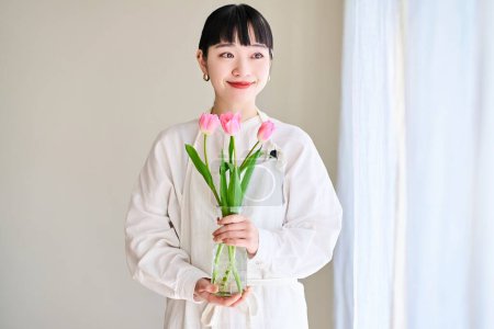 Téléchargez les photos : Jeune femme avec un vase de fleurs près de la fenêtre - en image libre de droit