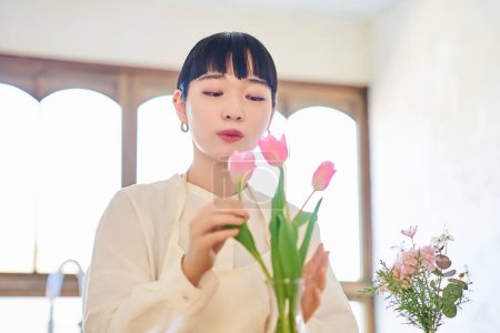Mujer joven disfrutando de flores en un jarrón en la habitación