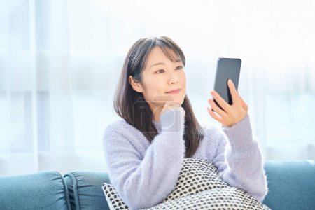 Téléchargez les photos : Jeune femme regardant l'écran du smartphone dans la chambre - en image libre de droit