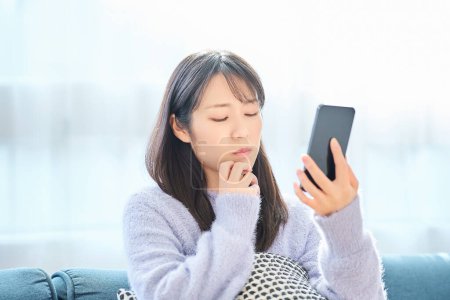 Junge Frau blickt mit enttäuschtem Gesichtsausdruck auf Smartphone im Raum