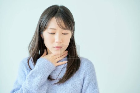 A young woman feels discomfort in her throat indoors