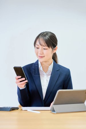 Une jeune femme en costume actionnant un smartphone devant un fond blanc