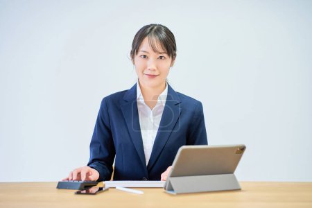 A woman in a suit operating a computer in front of a white background