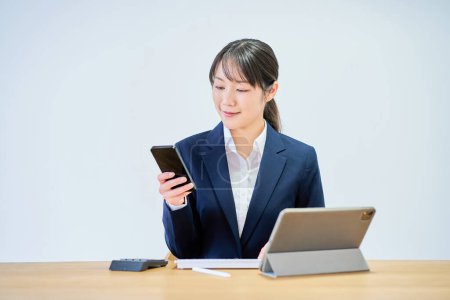 Téléchargez les photos : Une jeune femme en costume actionnant un smartphone devant un fond blanc - en image libre de droit