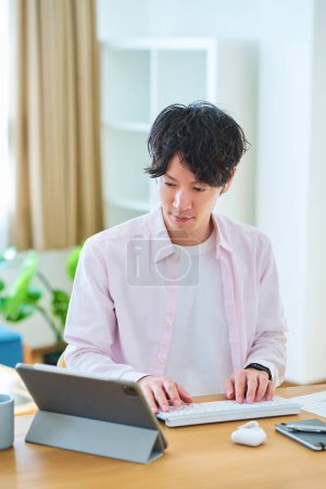 Téléchargez les photos : Jeune homme opérant un ordinateur dans sa chambre pendant la journée - en image libre de droit