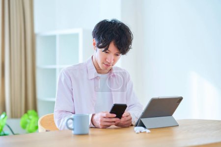 Photo for Young man comparing tablet PC and smartphone indoors - Royalty Free Image
