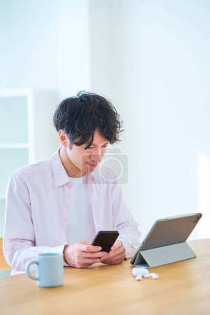 Téléchargez les photos : Jeune homme comparant tablette PC et smartphone à l'intérieur - en image libre de droit