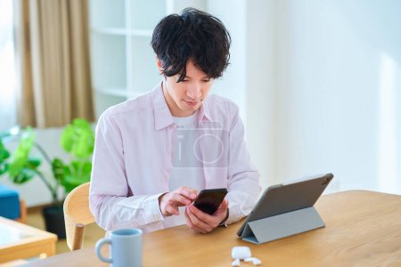 Photo for Young man comparing tablet PC and smartphone indoors - Royalty Free Image