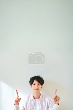 Téléchargez les photos : Jeune homme pointant vers le haut devant un fond blanc - en image libre de droit