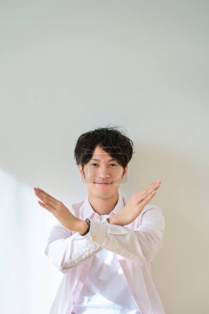 A young man making a NG sign in front of a white background
