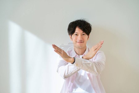 A young man making a NG sign in front of a white background