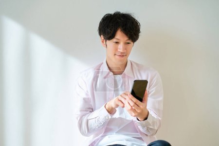 Téléchargez les photos : Jeune homme opérant un smartphone devant un fond blanc - en image libre de droit