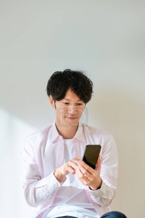 Young man operating a smartphone in front of a white background
