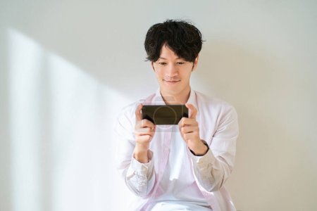 Hombre joven mirando la pantalla del teléfono inteligente en frente de fondo blanco