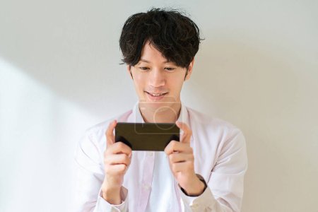 Junger Mann blickt auf Smartphone-Bildschirm vor weißem Hintergrund