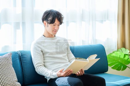 Téléchargez les photos : Jeune homme lisant un livre dans la chambre - en image libre de droit