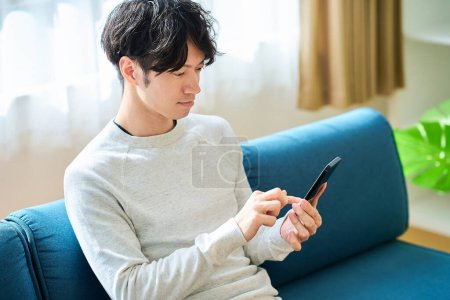 Photo for Young man holding a smartphone indoors - Royalty Free Image