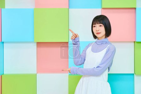 Photo for Colorful background with smiling young woman in pointing pose - Royalty Free Image