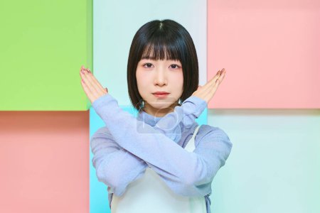 Colorful background with a young woman with a serious expression giving an NG sign
