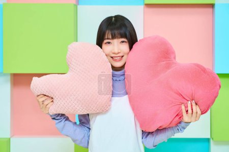 Téléchargez les photos : Jeune femme tenant un coussin en forme de cœur dans la chambre - en image libre de droit