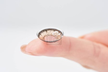 Woman's fingers with colored contact lenses and white background