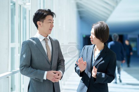 Téléchargez les photos : Homme et femme en costume ayant une conversation dans le couloir - en image libre de droit