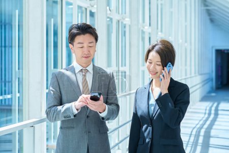 A man and a woman in suits operate a smartphone with a smile