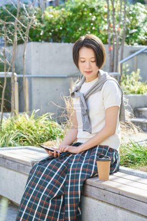 A woman using a smartphone while drinking coffee outdoors
