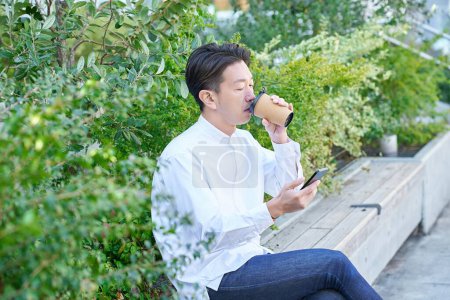 A man operating a smartphone while drinking coffee outdoors