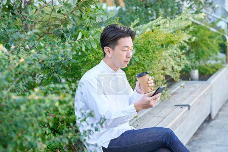 A man operating a smartphone while drinking coffee outdoors