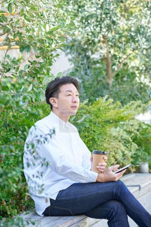 Foto de Un hombre que opera un teléfono inteligente mientras bebe café al aire libre - Imagen libre de derechos