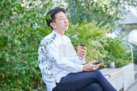 Ein Mann bedient ein Smartphone, während er draußen Kaffee trinkt