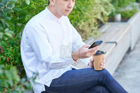 Un homme maniant un smartphone tout en buvant du café à l'extérieur