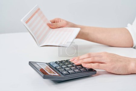 A woman holding a bank account passbook and using a calculator