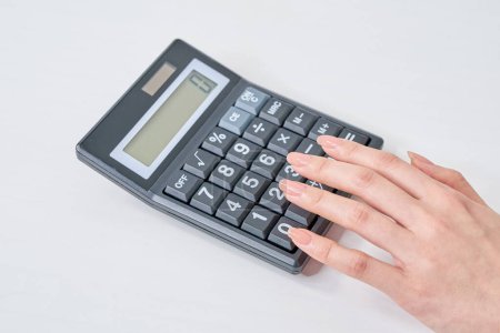 Mano de una mujer usando una calculadora y fondo blanco