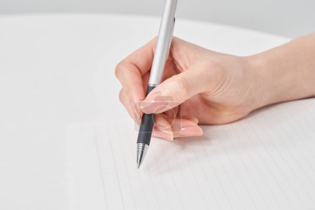 Hand einer Frau, die einen Stift hält und auf ein Notizbuch schreibt