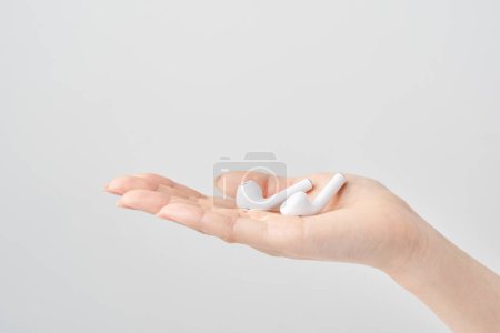 Woman's hand holding white wireless earphones and white background