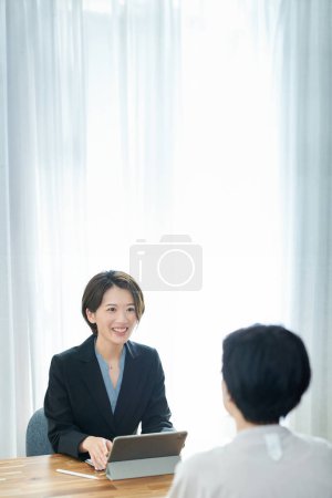 Una mujer con un traje sonriendo y explicándole a una mujer vestida de civil