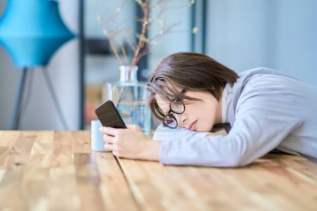 Eine Frau, die ein Smartphone bedient, sieht müde im Raum aus