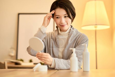 Eine Frau überprüft sich mit einem Handspiegel in einem Raum mit warmem Licht