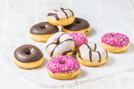 Téléchargez les photos : Donuts colorés, Berlinois, Krapfen avec glaçage au sucre et chocolat sur fond blanc en bois, vertical avec espace de copie - en image libre de droit