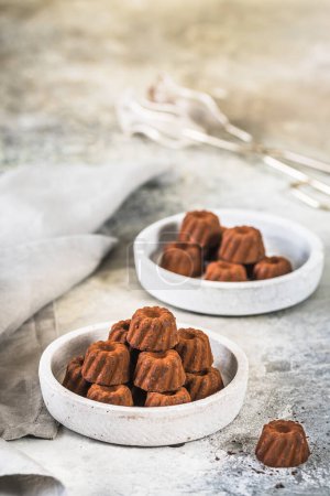 Téléchargez les photos : Pralines au chocolat en forme de petites tartes Guglhupf, saupoudrées de cacao, sur fond gris clair, verticales avec espace de copie - en image libre de droit