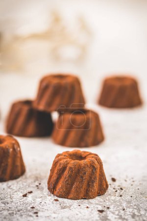 Téléchargez les photos : Pralines au chocolat sous la forme de petits gâteaux Bundt saupoudrés de cacao, sur un fond gris clair, se concentrer sur un seul chocolat au premier plan, vertical avec espace de copie - en image libre de droit