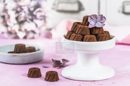 Téléchargez les photos : Pralines au chocolat en forme de petits gâteaux Bundt, saupoudrés de cacao, sur fond rose clair, décorées de fleurs d'hortensia - en image libre de droit