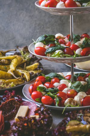 Photo for Italian starter buffet with tomatoes and mozzarella, grilled pepperoni and sausage specialties, vertical - Royalty Free Image